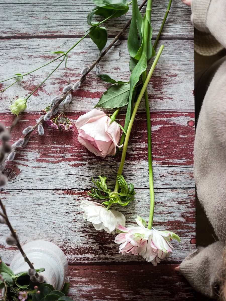 Mains d'une fleuriste composant un arrangement de fleurs blanches et roses sur un plan en bois